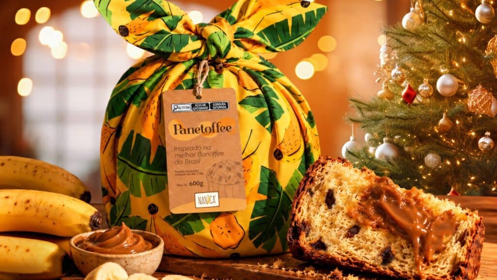 Panetoffe da Nanica em embalagem decorada, com fatia de panetone e doce de leite de banana ao lado de frutas e decoração natalina