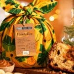 Panetoffe da Nanica em embalagem decorada, com fatia de panetone e doce de leite de banana ao lado de frutas e decoração natalina