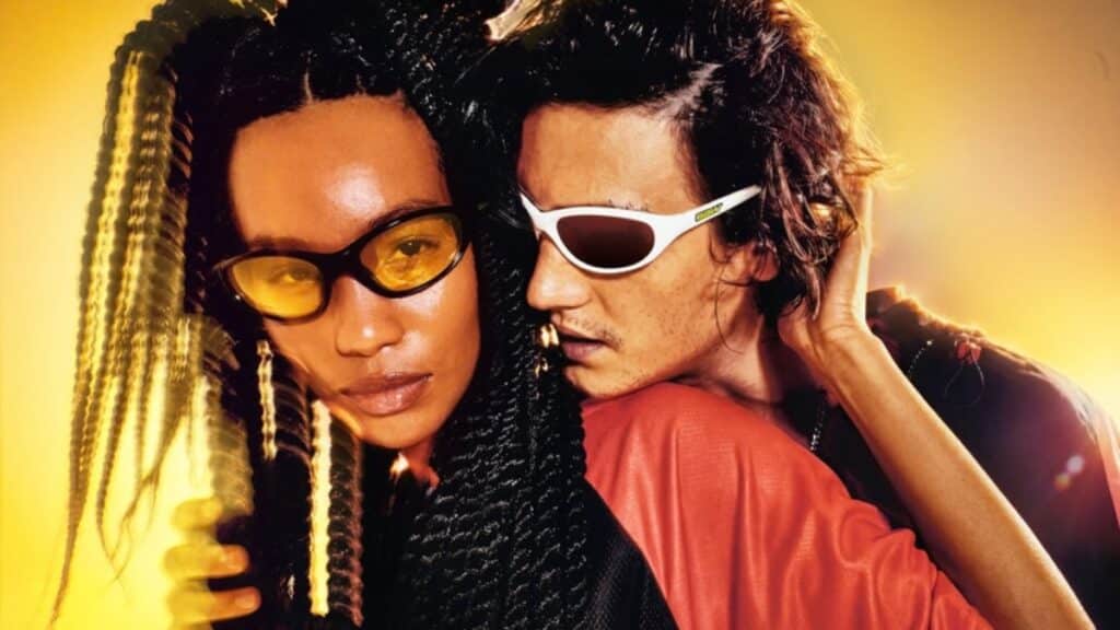 Casal usando óculos Chilli Beans em estilo rave anos 1990, com iluminação dourada e vibe streetwear