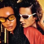 Casal usando óculos Chilli Beans em estilo rave anos 1990, com iluminação dourada e vibe streetwear