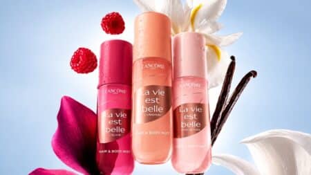 La Vie Est Belle Lancôme: body splash e hair & body mist Frascos de body splash e hair & body mist La Vie Est Belle da Lancôme com flores em fundo claro.
