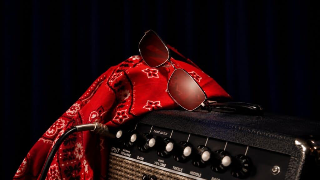 Óculos vermelhos na coleção Rock Fellas da Chilli Beans Chapéu e óculos vermelhos com estampa sobre amplificador de guitarra, na coleção Rock Fellas da Chilli Beans