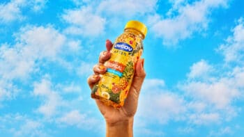 Engov After Tropical: edição limitada para o verão Mão segurando embalagem de Engov After sabor Tropical, com fundo de céu azul e nuvens.