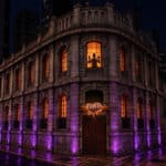 Fachada iluminada da Fábrica Assombrada da Fanta à noite, com luzes roxas e janela em clima de Halloween