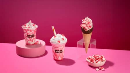 Parceria Fini e Brasil Cacau com sobremesas e chocolates Sobremesas e chocolates da collab Fini e Brasil Cacau em fundo rosa, com copos e cone decorados com morango