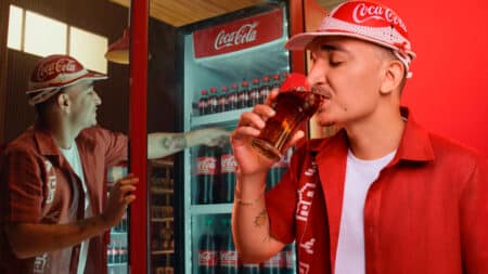 João Gomes brinda com garrafas retornáveis da Coca-Cola João Gomes em campanha da Coca-Cola, brindando com garrafas retornáveis em um estabelecimento.