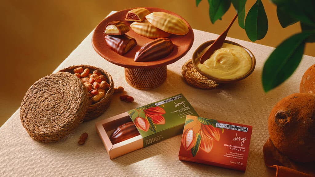 Dengo Chameguinhos: chocolates recheados Dengo Chocolates Dengo Chameguinhos recheados com chocolate e amendoim, apresentados ao lado de frutas e folhas.