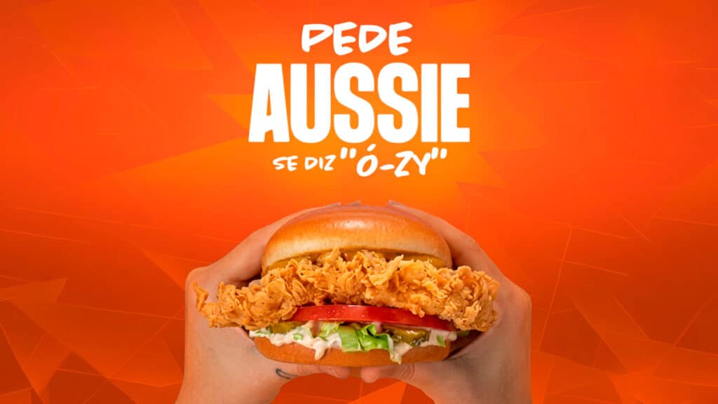 Cartaz da campanha da Aussie com hambúrguer na mão e texto “Pede Aussie” e “Se diz ‘ô-zí’”.