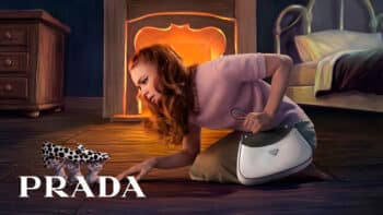 Campanha de Natal 2026 da Prada com ilustração e bolsa Campanha de Natal da Prada com mulher deitada ao lado de bolsa e cenário iluminado com luz laranja ao fundo.