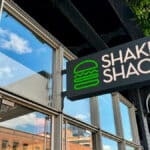 Placa da Shake Shack na entrada de uma loja, anunciando a chegada da marca ao Brasil.