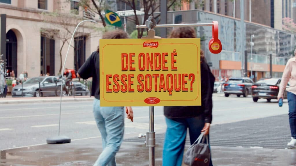Vitarella destaca sotaques com placa “De onde é esse sotaque?” Pessoa em rua com placa “DE ONDE É ESSE SOTAQUE?” em campanha da Vitarella para o Dia do Nordestino.