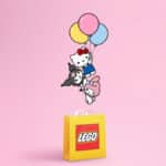 Ilustração com personagens Hello Kitty e amigos sobre bloco LEGO amarelo em fundo rosa, com balões coloridos no topo.