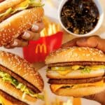 Pessoas segurando hambúrgueres do McDia Feliz 2026 em comemoração à arrecadação de R$ 28,5 milhões.