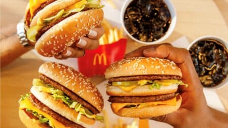 McDia Feliz 2026: hambúrgueres e arrecadação de R$ 28,5 milhões Pessoas segurando hambúrgueres do McDia Feliz 2026 em comemoração à arrecadação de R$ 28,5 milhões.