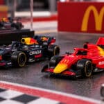 Miniaturas de carros de Fórmula 1 da Red Bull e McDonald's em pista, com logotipo do McDonald’s ao fundo.