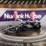 Nubank House com réplica da Mercedes-AMG F1 em ambiente de exposição, com painel roxo e cadeiras ao fundo.