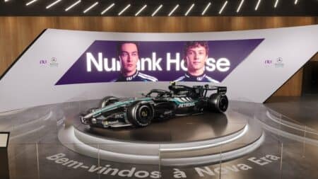 Nubank House com réplica da Mercedes-AMG F1 Nubank House com réplica da Mercedes-AMG F1 em ambiente de exposição, com painel roxo e cadeiras ao fundo.