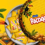 Lata colecionável de Paçoquita Original com ilustrações de pássaros e animais sobre fundo amarelo, com pacotes ao redor.
